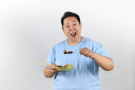 Portrait of Asian man holding a flavorful plate of Traditional Indonesian satayの写真素材