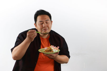 Excited Asian man presenting a plate of authentic Indonesian fried rice, street food concept for culinary advertisingの写真素材
