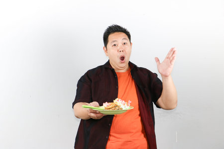 Excited Asian man presenting a plate of authentic Indonesian fried rice, street food concept for culinary advertisingの写真素材