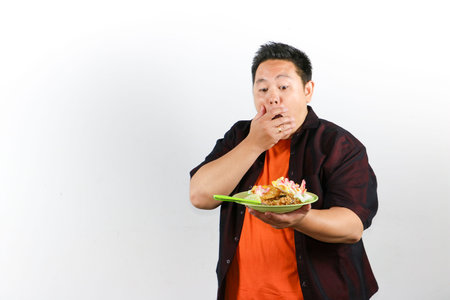 Happy Asian traveler enjoying authentic Indonesian nasi goreng or fried rice with egg and crackers, culinary tourism concept.の写真素材