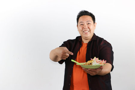 Excited Asian man presenting a plate of authentic Indonesian fried rice, street food concept for culinary advertisingの写真素材