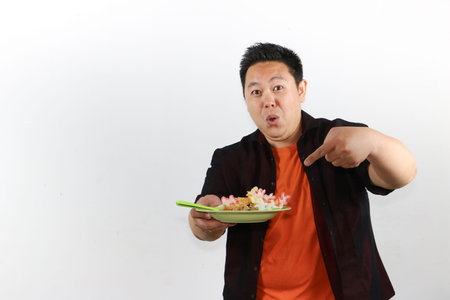 Young Asian man enjoying delicious Indonesian nasi goreng with crackers and egg, authentic Southeast Asian culinary tourismの写真素材