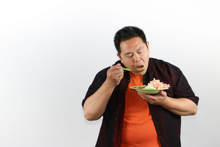 Cheerful Asian man holding a plate of authentic Indonesian fried rice, culinary exploration and lifestyle conceptの写真素材