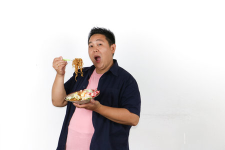 Hungry Asian man tasting tasty mie goreng served with fried egg and crackers, Indonesian traditional...