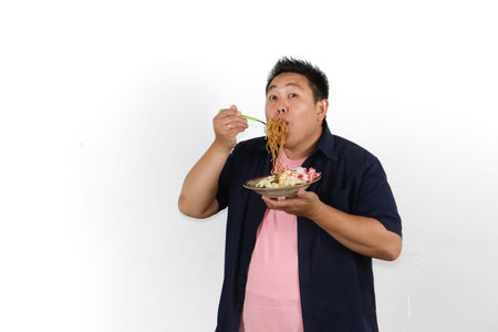 An Asian man enjoys a mouthful of delicious authentic Indonesian fried noodles with egg and crackers