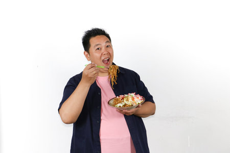 Hungry Asian man tasting tasty mie goreng served with fried egg and crackers, Indonesian traditional...