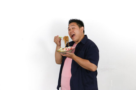 An Asian man enjoys a mouthful of delicious authentic Indonesian fried noodles with egg and crackers