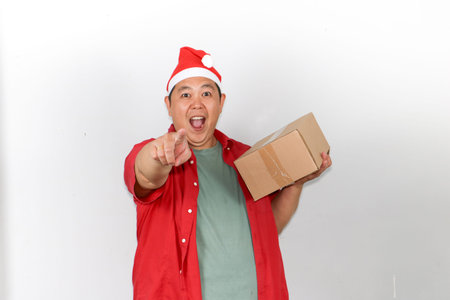 Portrait of a friendly asian guy in festive attire delivering a holiday package against a white...