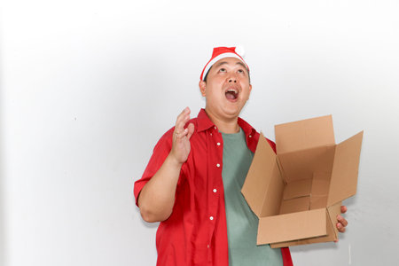 Smiling young asian man celebrating Christmas and New Year while carrying a taped cardboard delivery...