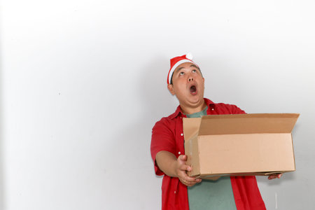 Smiling young asian man celebrating Christmas and New Year while carrying a taped cardboard delivery...