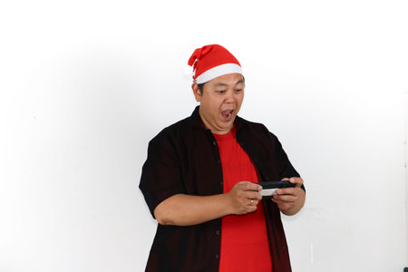 Happy Asian man in Santa hat showing phone screen for Christmas holiday promo isolated on white...