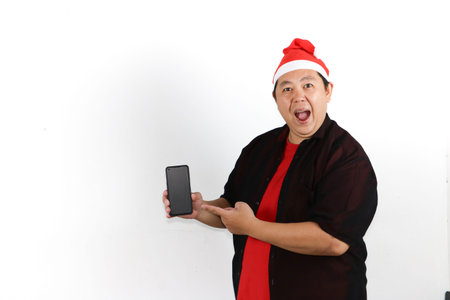 Surprised Asian man wearing Santa hat showing smartphone screen for Christmas and New Year online...