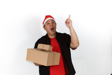 Cheerful Asian man in Santa hat holding mobile phone and showing excitement isolated on white...