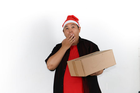 Cheerful Asian man in Santa hat showing smartphone screen and surprise gesture for Christmas holiday...