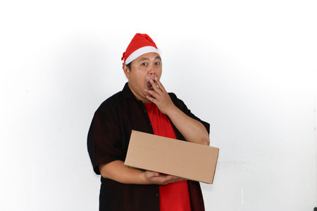 Cheerful Asian man in Santa hat showing smartphone screen and surprise gesture for Christmas holiday...