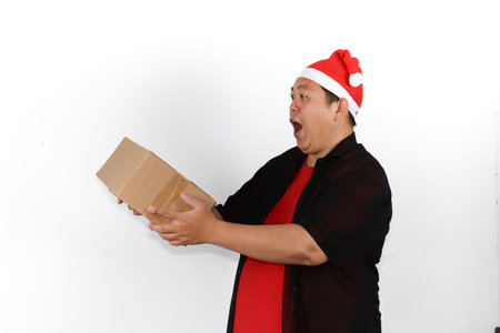 Portrait of cheerful Asian man in Santa hat holding cellphone and pointing to blank screen on white...