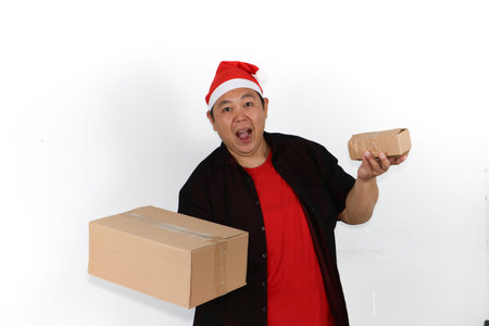 Portrait of cheerful Asian man in Santa hat holding cellphone and pointing to blank screen on white...