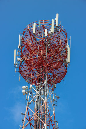 Low angle shot of a red telecommunication tower with several white antennas against a blue sky