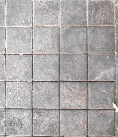 Detailed texture of industrial grey stone tiles featuring subtle cracks and outdoor debris on the...