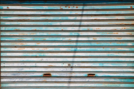 Close up of a weathered blue metal rolling shutter with several patches of brown rust