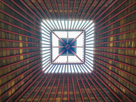 Modern pyramidal roof design featuring vibrant red rafters and natural wood planks in a geometric...