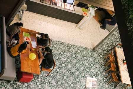 A top down view shows a family dining at a long wooden table in a busy food court