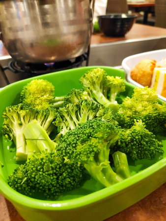 Fresh green broccoli florets served in a bright plastic bowl for a healthy steamboat meal preparationの写真素材