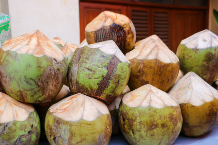 Pile of fresh green coconuts with decorative carved pointed tops displayed on a table in tropical...