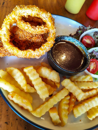 Appetizer platter featuring fried onion rings crinkle fries and a small bowl of dark dipping sauce
