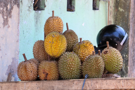Pile of fresh durian fruits with sharp thorns displayed on a wooden table at a roadside market