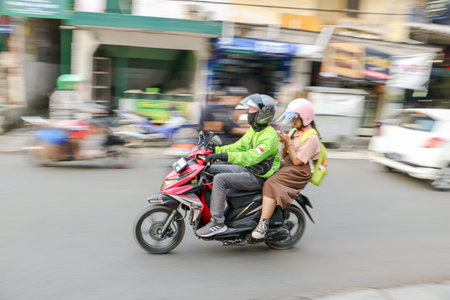 Grab driver wearing a green jacket and helmet riding a motorcycle on a busy street, Bandung,...