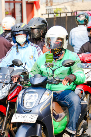 Grab driver wearing a green jacket and helmet riding a motorcycle on a busy street, Bandung,...