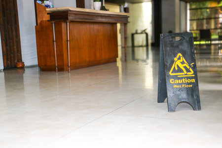 Black caution wet floor sign stands at the entrance of a restaurant with warm blurry lighting in backgroundのeditorial素材