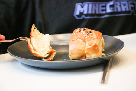A person uses a golden fork to pick up a piece of sliced Cromboloni pastry on a dark plate