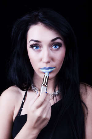 Beautiful young woman painting lips in blue colorの写真素材