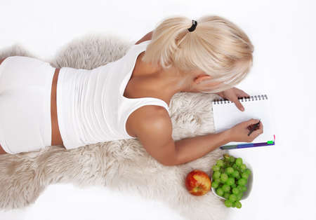 Portrait of a sexy blond woman writing in diary and lying on the floor.の写真素材