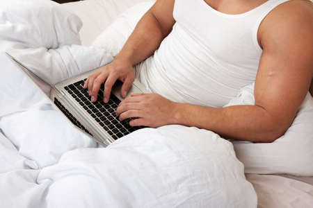 Young man using laptop at the bedtimeの写真素材