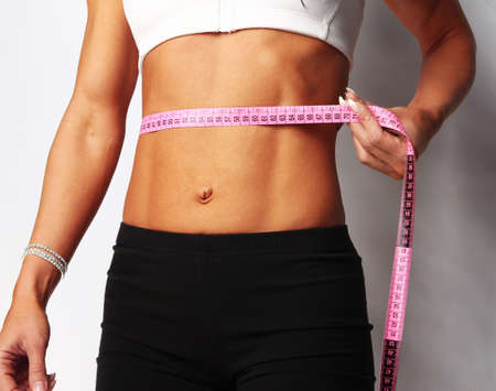 Closeup of young female measuring her waist, isolated on greyの写真素材