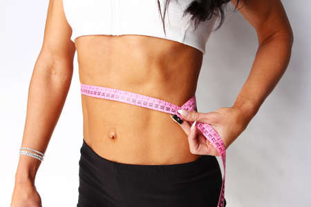 Closeup of young female measuring her waist, isolated on greyの写真素材