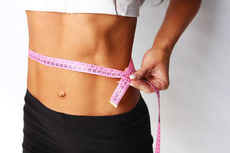 Closeup of young female measuring her waist, isolated on greyの写真素材