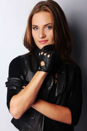 Portrait of beautiful brunette female wearing leather jacket and gloves, isolated on greyの写真素材