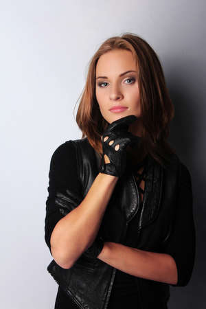 Portrait of beautiful brunette female wearing leather jacket and gloves, isolated on greyの写真素材