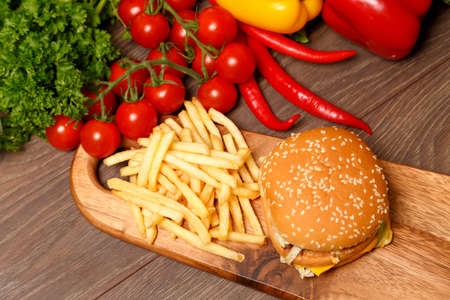 Junk food on a wooden board surrounded by healthy vegetables