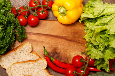 Wooden cutting board surrounded by vegetables and two pieces of breadの写真素材