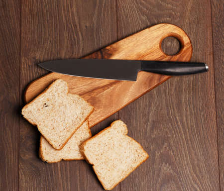 Knife on a cutting board and three pieces of breadの写真素材