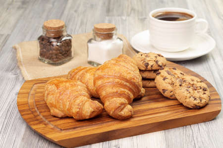 A cup of black coffee and some pastries on a wooden board