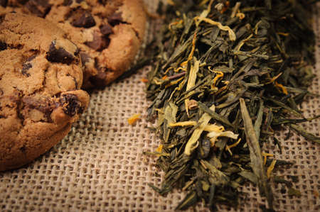 Dry tea leaves and two cookies on a linen cloth