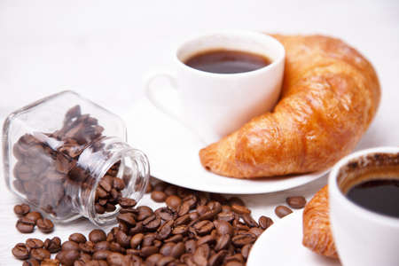 A white cup of coffee with croissant and coffee beansの写真素材