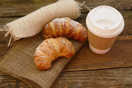 Two croissants and coffee-to-go in a rustic setting Two croissants and coffee-to-go in a rustic setting