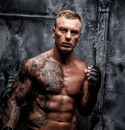 Muscular strong male with tattoo poses over the wallの写真素材